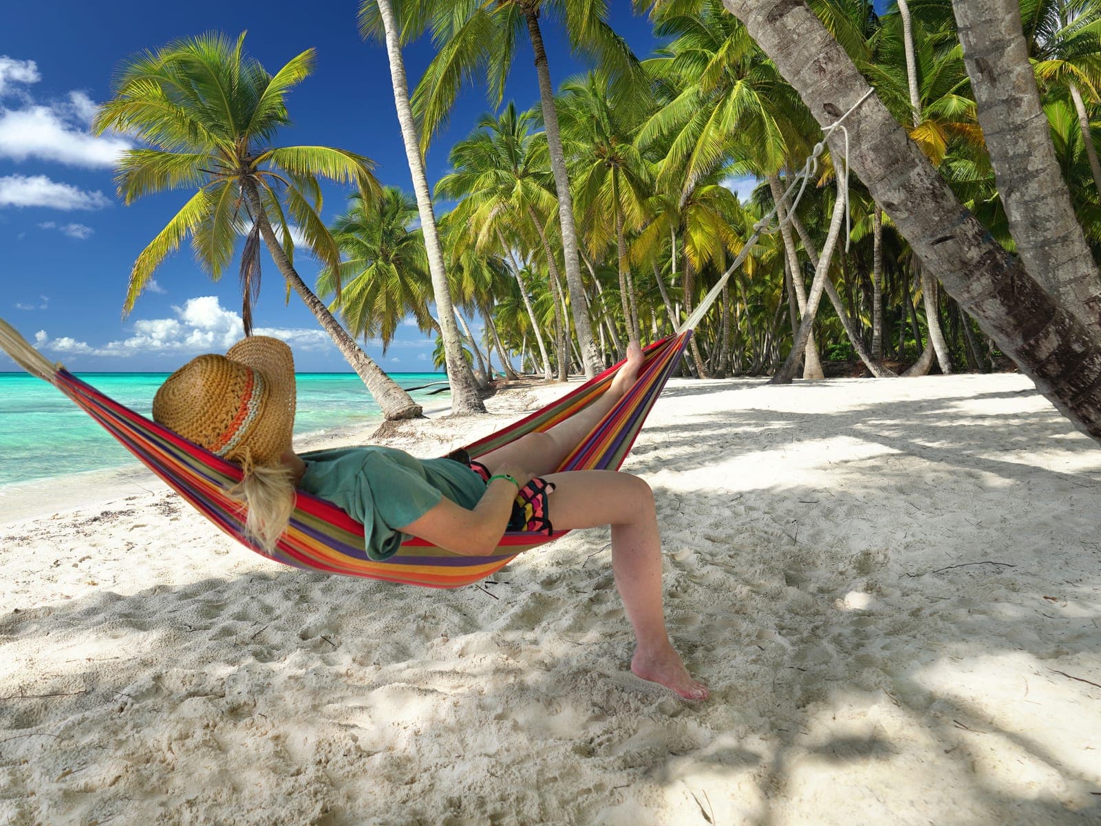 A traveller resting in a hammock between leaning palms on white sand in Punta Cana, turquoise water behind.